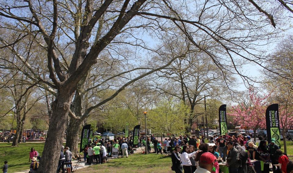 crowds of people in a tree-lined park visiting booths distributed around the park