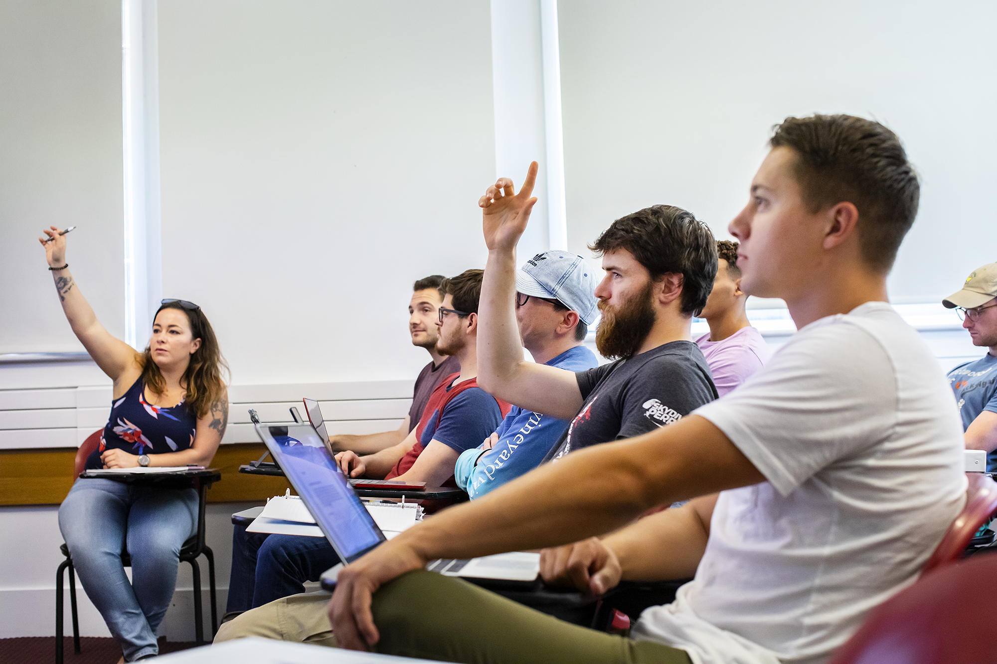 Students face forward in a classroom, a few raising hands