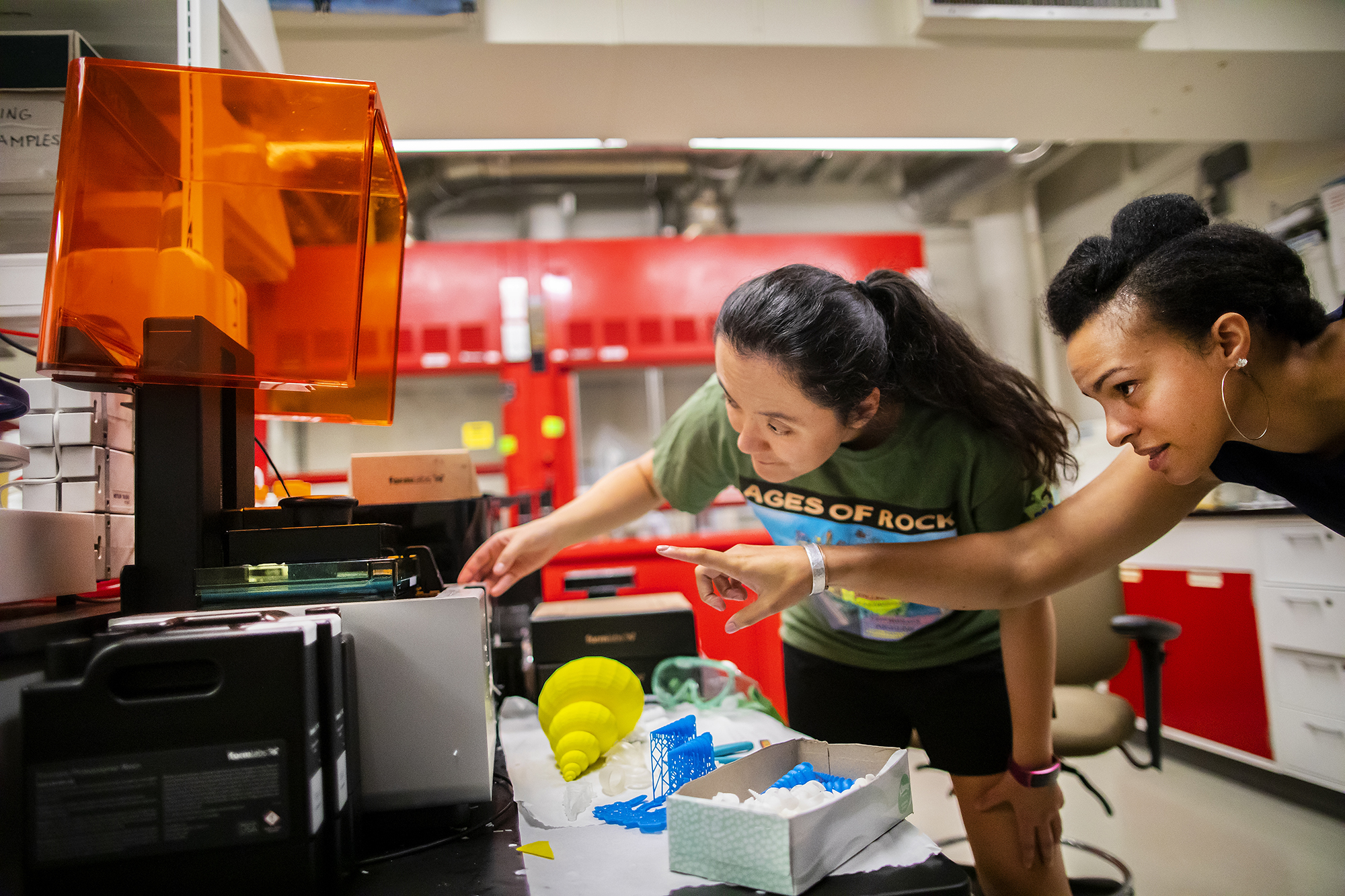 Two scientists point to and inspect the output of a 3D printer in a lab