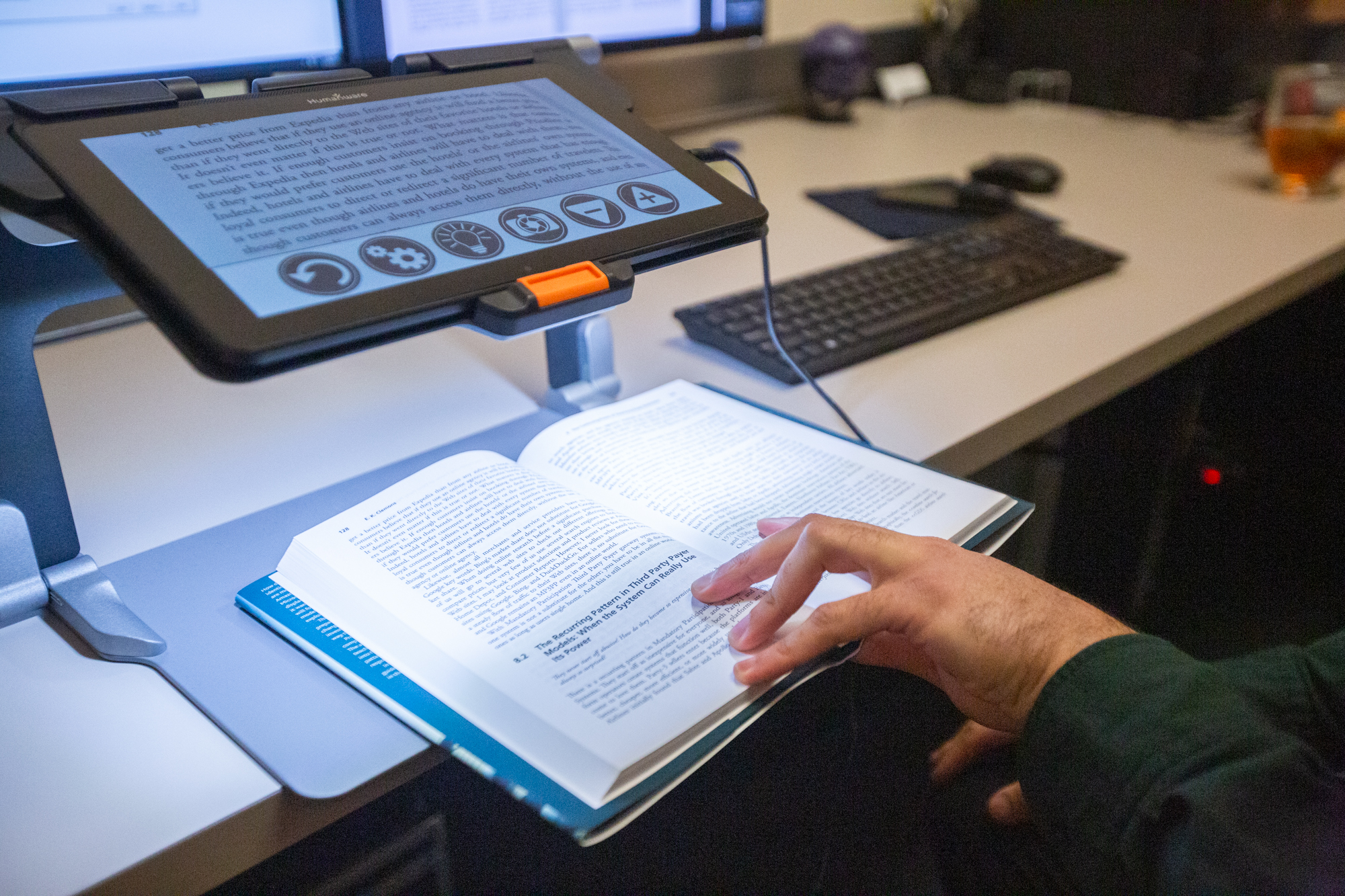 A hand on an open book attached to an assisted reading computer at the Weingarten assisted learning center