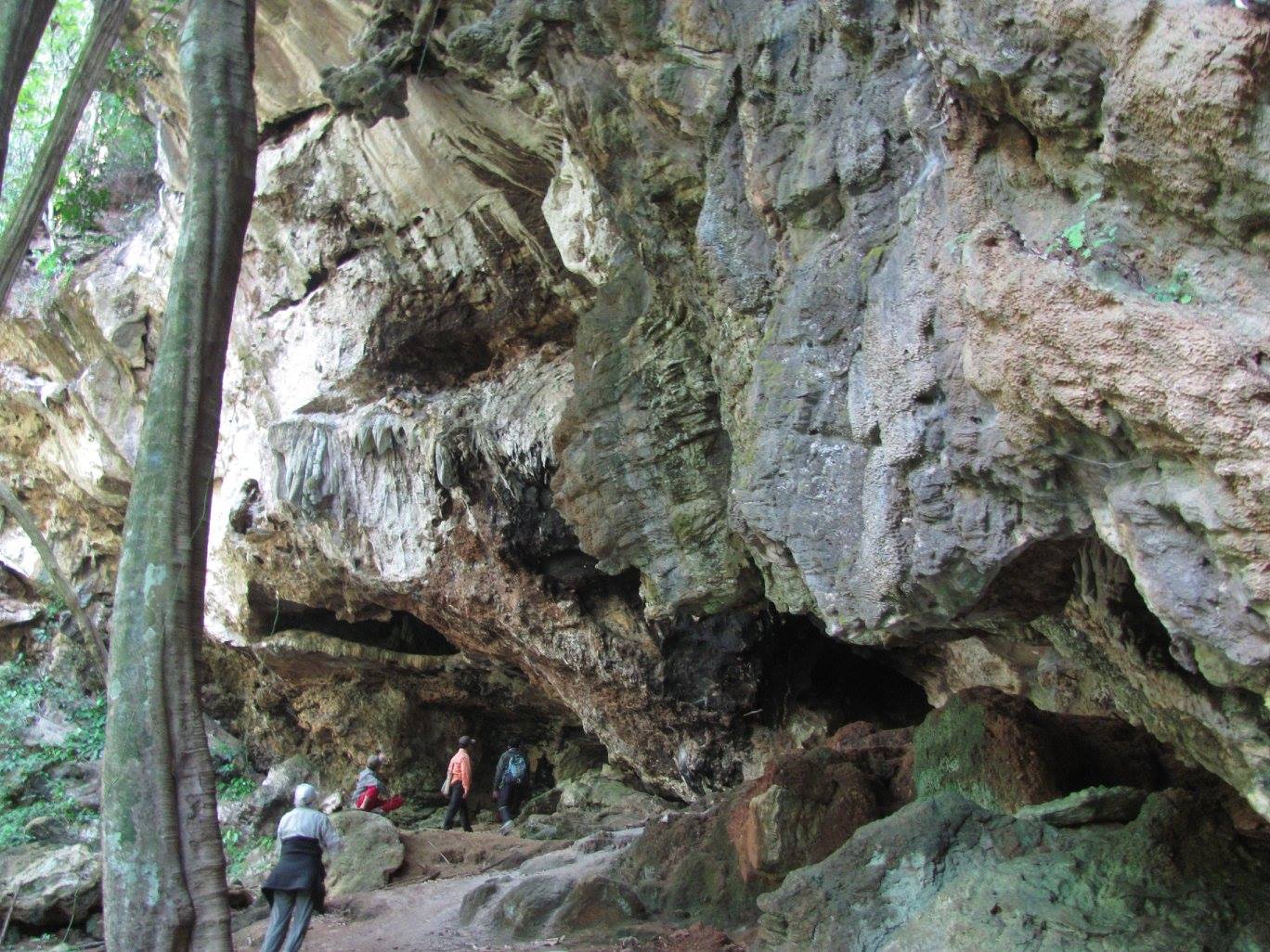 A massive rock structure with an opening at the base where people are walking. 