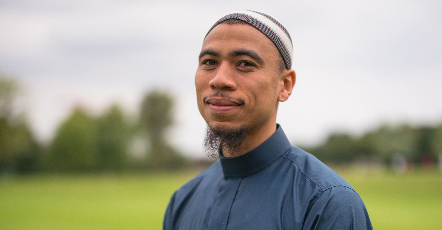 Ibrahim Jaaber wears a Muslim hat and garb in front of an open field.