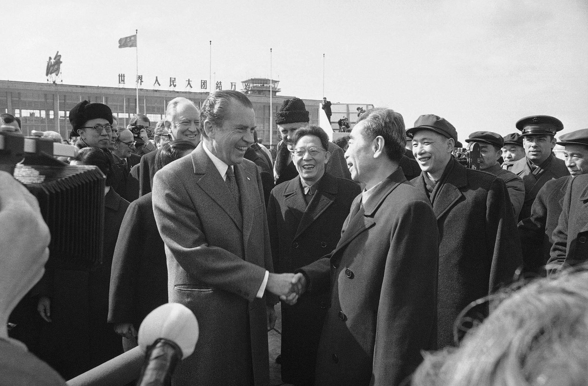 Richard Nixon shakes hands with Chinese Premier Chou En-Lai with smiling lookers surrounding them