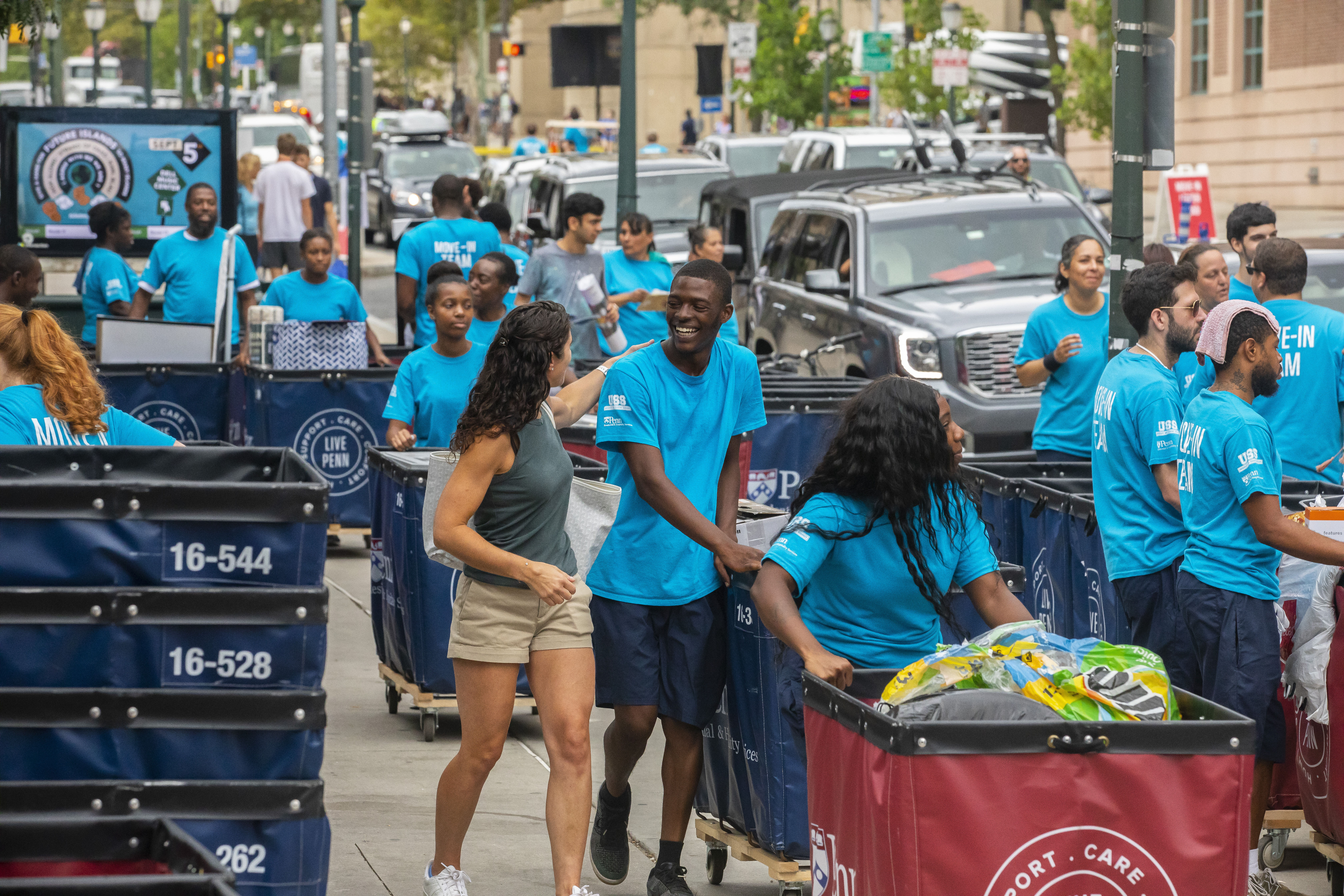 Crowded sidewalk with students and volunteers pushing moving carts. 