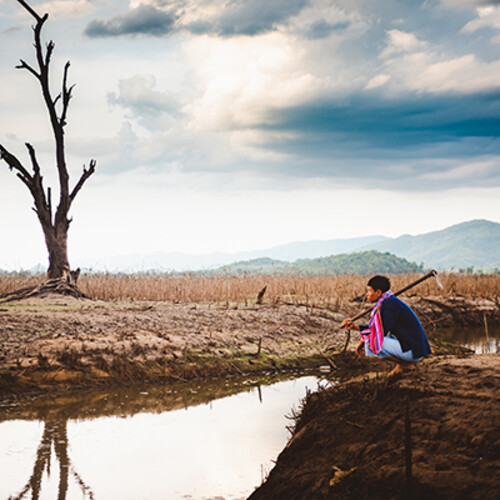 farmer sits on cracked earth near drying water source