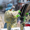 A health care worker in personal protective gear swabs a person in a vehicle at a drive-up COVID testing site.