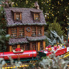 Holiday Garden Railway on display with modeled cars and houses, wrapped in lights.