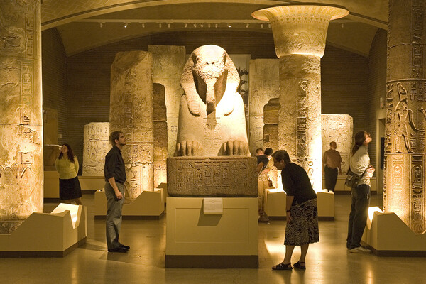 The Sphinx of Rameses II centered at a showroom of Penn Museum with people walking around and looking at the displays.
