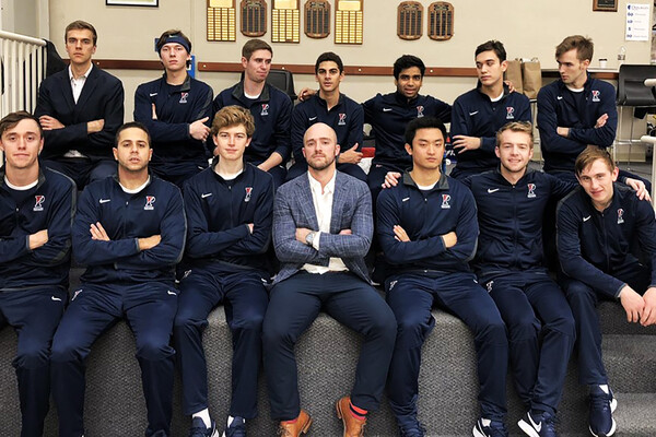 Men's squash players and the head coach pose on a bench