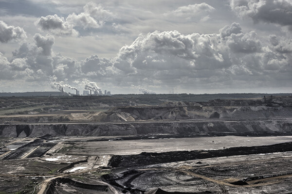 Wide-angle view of a heavily mined landscape with a refinery or energy facility in the background.