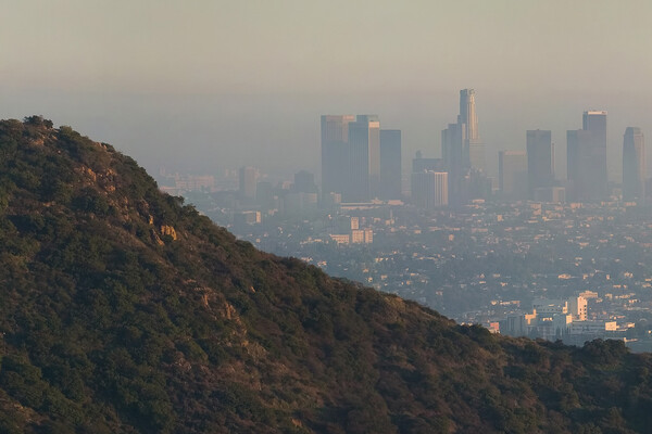 A mountain foregrounds the Los Angeles skyline, shrouded in haze