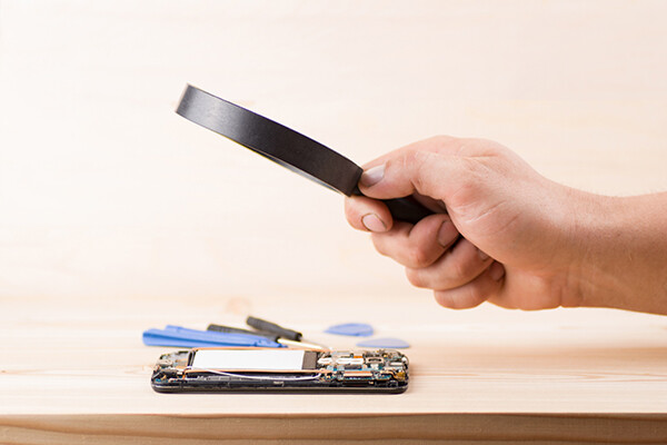 Hand holding a magnifying glass over back of disassembled smartphone