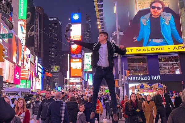 Young man holding a camera jumps above a trash can in the middle of busy Times Square
