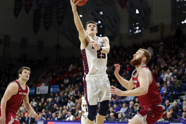 Forward AJ Brodeur of the men's basketball team lays the ball in the basket between two defenders at the Palestra.