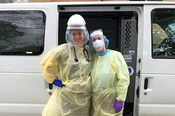 Two medical workers in full PPE standing outside a medical transit van.