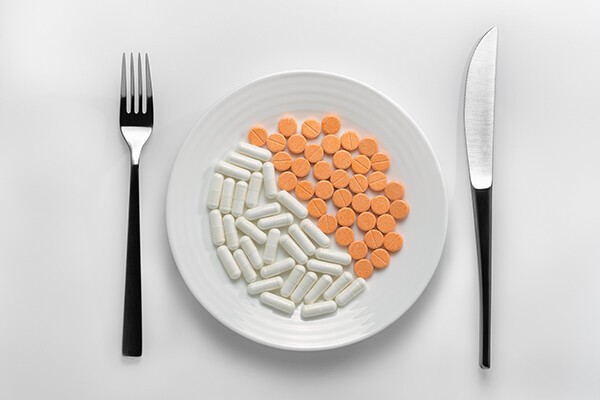A table setting with a fork, knife, and plate covered in two kinds of prescription pills.