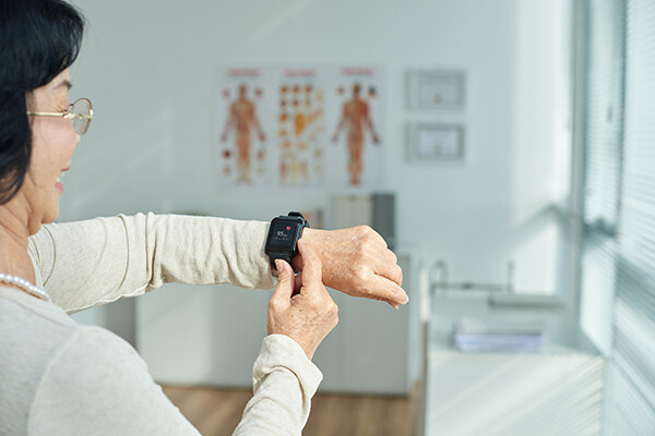 Older person in doctor’s office smiling while using a fitness tracker.