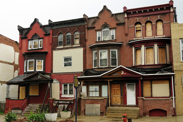 Row of three-story rowhouses in Philadelphia, some windows boarded up.