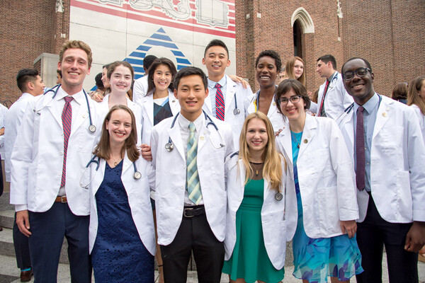 A group of Penn Med students in white coats standing on the steps outside Penn Commons.