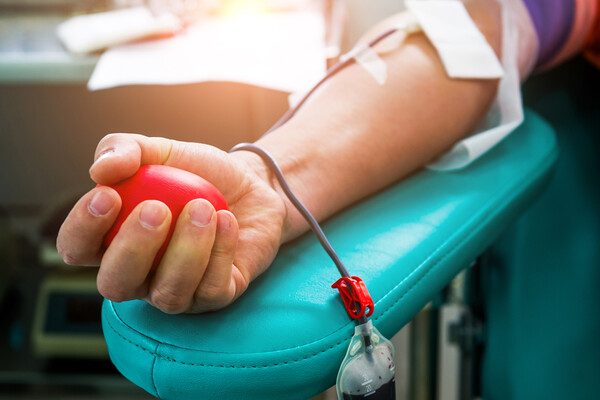 A blood donor squeezes a ball while their arm lays on an armrest 