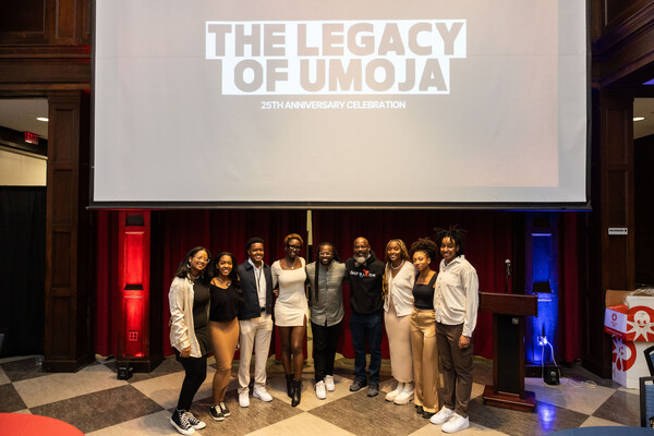 Nine people stand underneath a screen that reads "The Legacy of UMOJA 25th anniversary celebration"